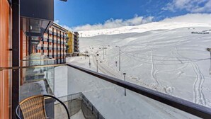 Pendenza innevata per lo sci con un edificio dotato di un balcone in vetro e una seggiovia.
