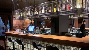 Eine Bar mit einer Holztheke, mehreren Barhocker und einer Flaschenauslage hinter einem Drahtgitter.