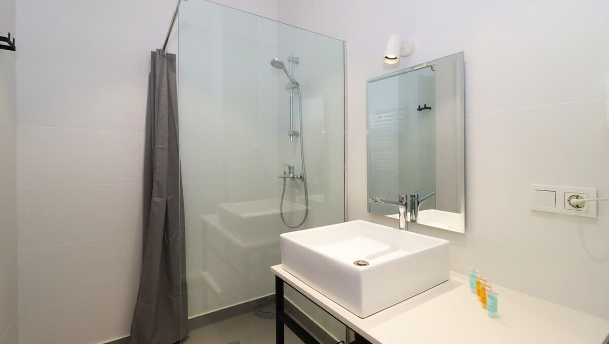 A modern bathroom with a glass shower enclosure, a white sink, and a mirror above it.
