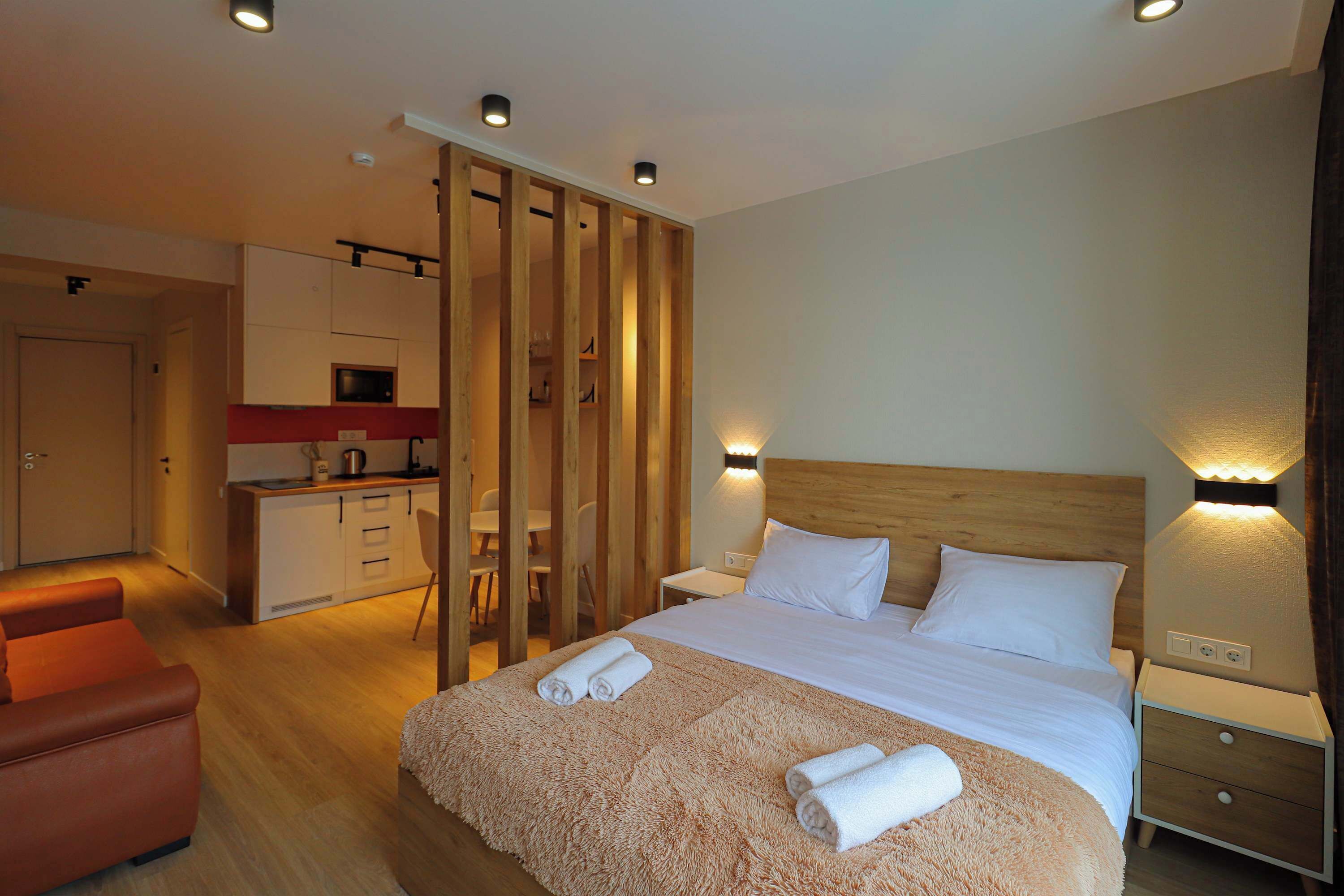 Een hotelkamer met een bed, nachtkastjes, een houten hoofdeinde, een bank, een kitchenette en een schuifdeur.