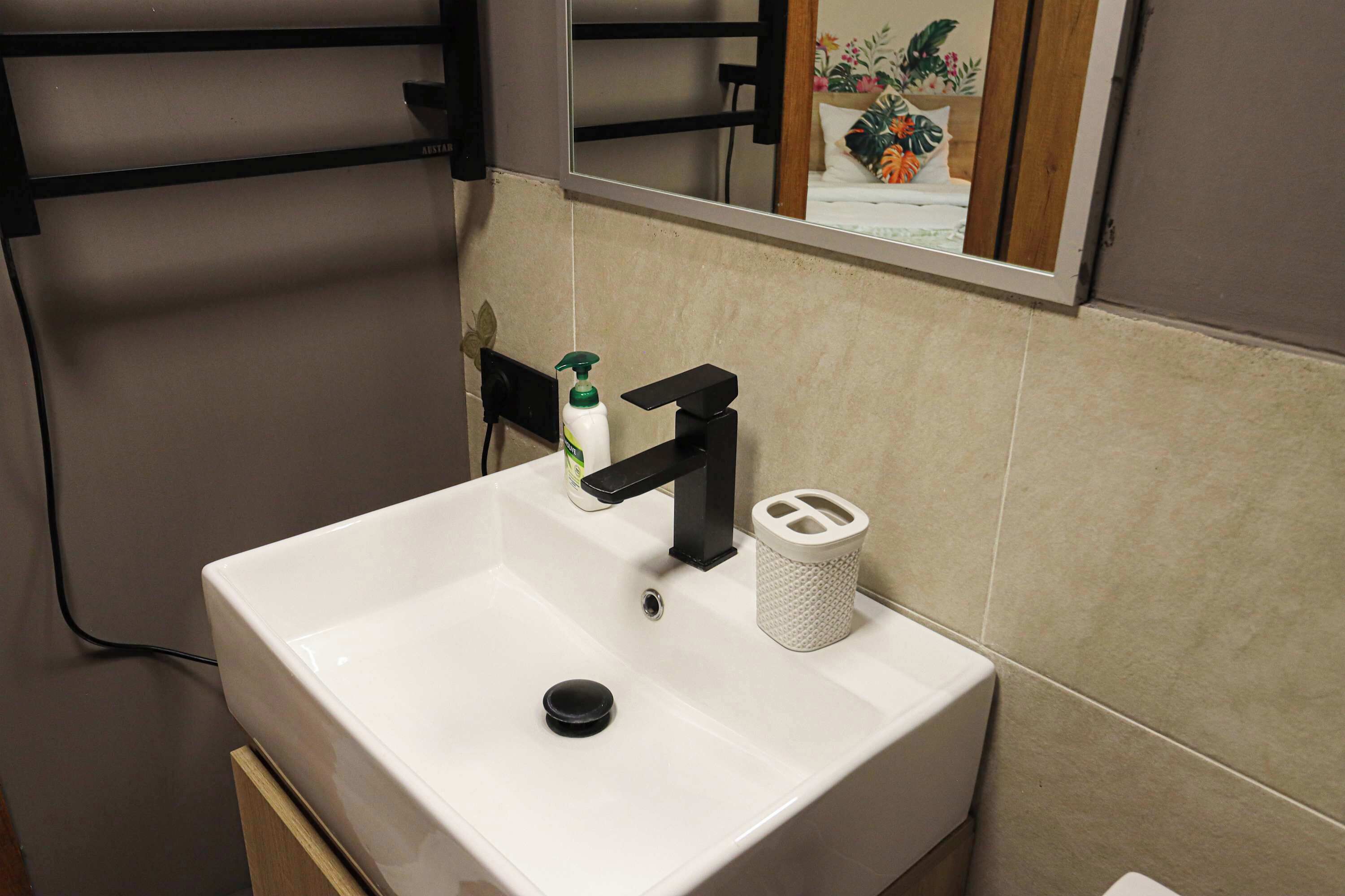 Un baño con un lavamanos blanco, grifo negro y un espejo encima.