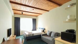 A hotel room with a wooden ceiling, a bed with a blue headboard, a grey sofa, a wooden table, and a TV. - Neo Gudauri Sylish Studio - Managed By Wehost (Gudauri)