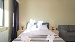 A hotel room with a large bed, two bedside tables with lamps, a grey sofa, and a window with curtains. - Neo Gudauri Sylish Studio - Managed By Wehost (Gudauri)