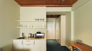A compact kitchen with a microwave, kettle, and glassware on shelves. A dining table with chairs is in the adjacent room. - Neo Gudauri Sylish Studio - Managed By Wehost (Gudauri)