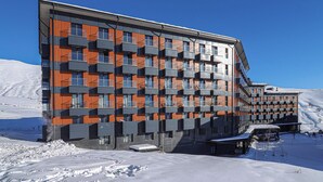 A modern multi-story hotel with a distinctive facade featuring alternating orange and gray panels. - Neo Gudauri Sylish Studio - Managed By Wehost (Gudauri)