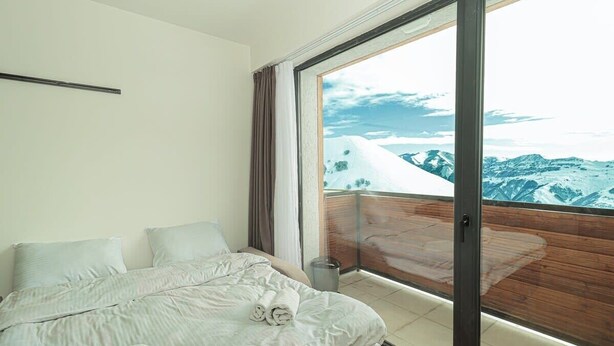 Un dormitorio con una cama grande, vistas de montañas nevadas a través de un ventanal corredero y un balcón de madera.