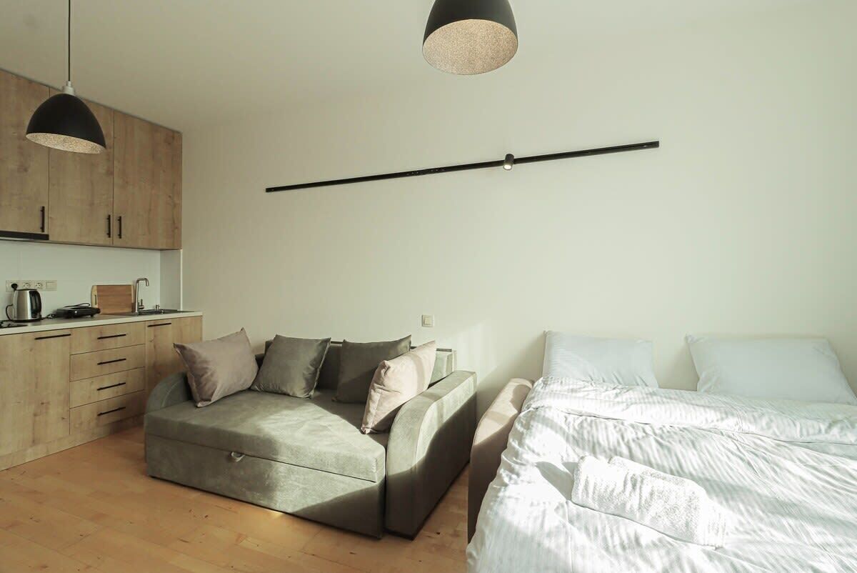 A compact living space with a sofa, a bed, a kitchenette, and pendant lighting.