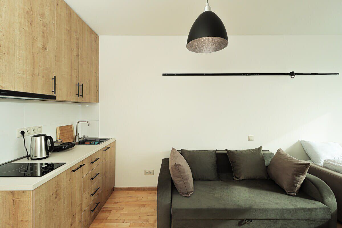 Un espace de vie compact comprenant un coin cuisine, un canapé et un luminaire suspendu.