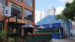 Een bedrijfsgebouw met een blauwe gevel, een terras met parasols en een hekwerk.