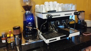 Een koffieapparaat met meerdere kopjes en een koffiemolen, plus een melkopschuimer op een aanrecht.