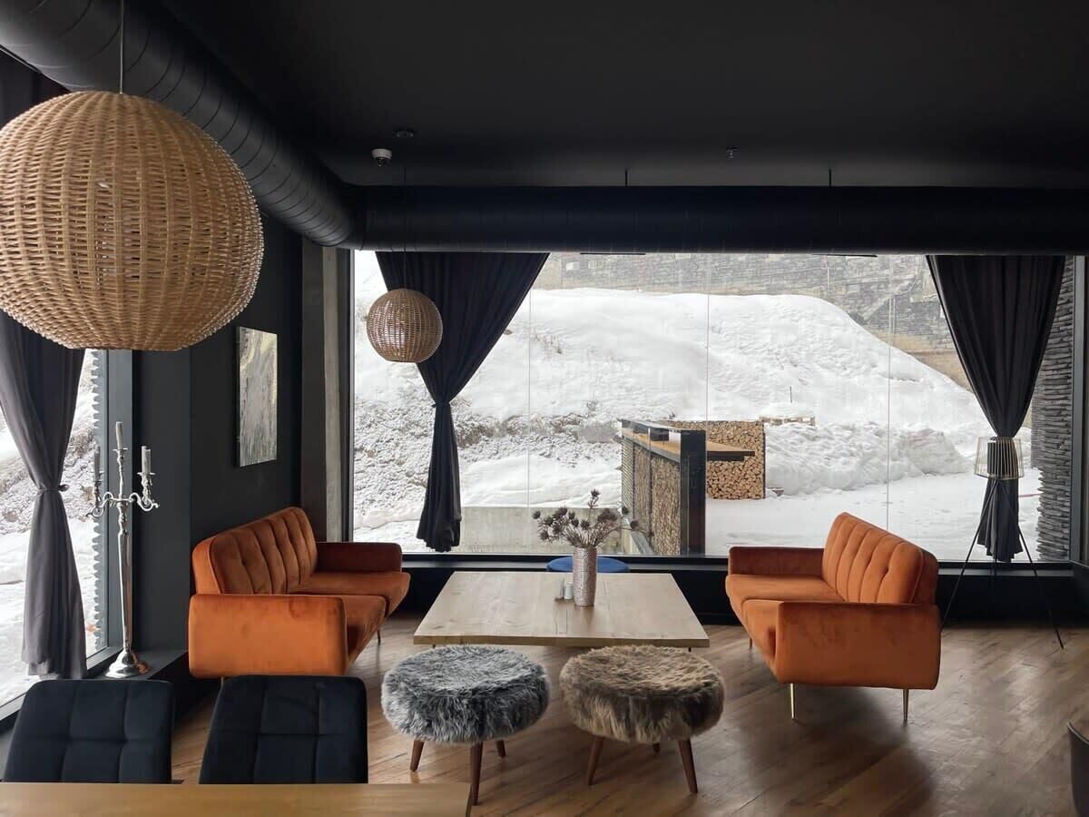 A modern living room with a large window, two orange sofas, a wooden coffee table, and a wicker pendant light.