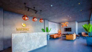 Um lobby moderno com uma receção em mármore, área de estar e lustres suspensos.