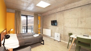 A hotel room with a bed, a desk, a chair, a TV, and a window with curtains. - Stylish Ski-In/Out Apt- Mountain Views - By Wehost (Gudauri)