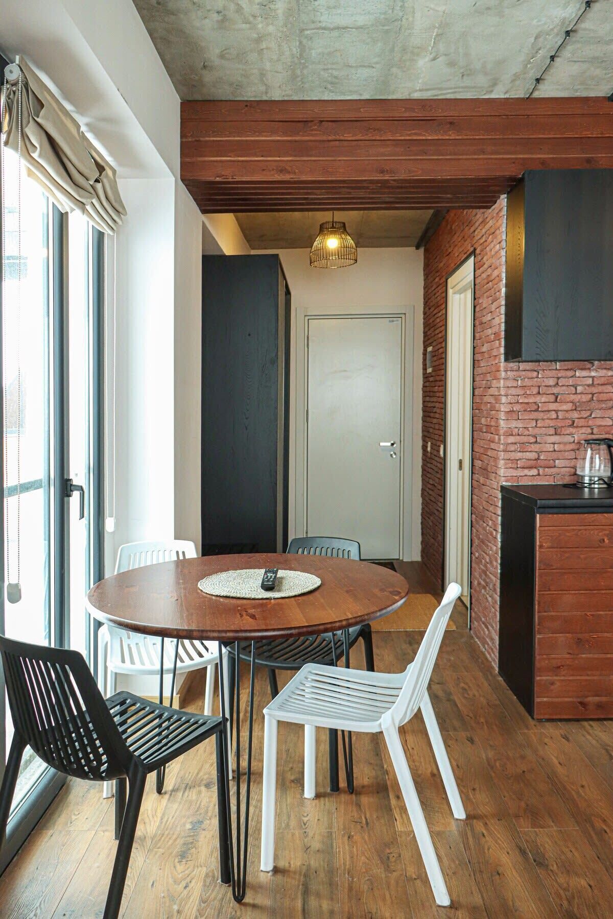 Een eetgedeelte met een ronde houten tafel, twee zwarte stoelen en twee witte stoelen. Daarboven hangt een lamp.