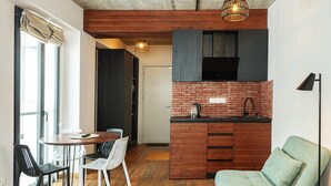 A compact kitchen with a brick backsplash, a dining area with a round table and chairs, and a green sofa. - New Gudauri Studio with Balcony By Wehost (Gudauri)