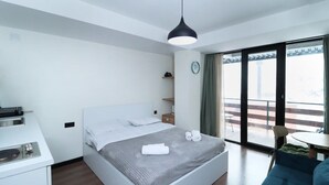 A modern hotel room with a bed, a desk, a chair, a balcony with a view, and a hanging light fixture. - Gudauri Cozy Studio - Adventure Ready - By Wehost (Gudauri)
