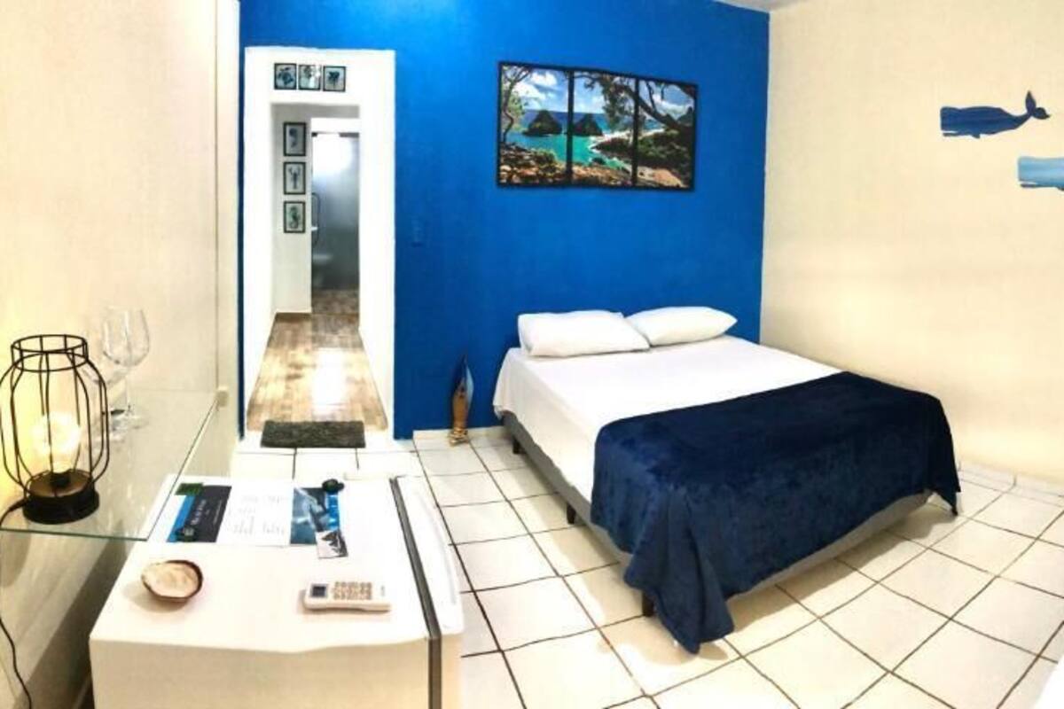 Habitación de hotel con cama, escritorio con lámpara y pared decorada con una imagen de playa y dos ballenas.