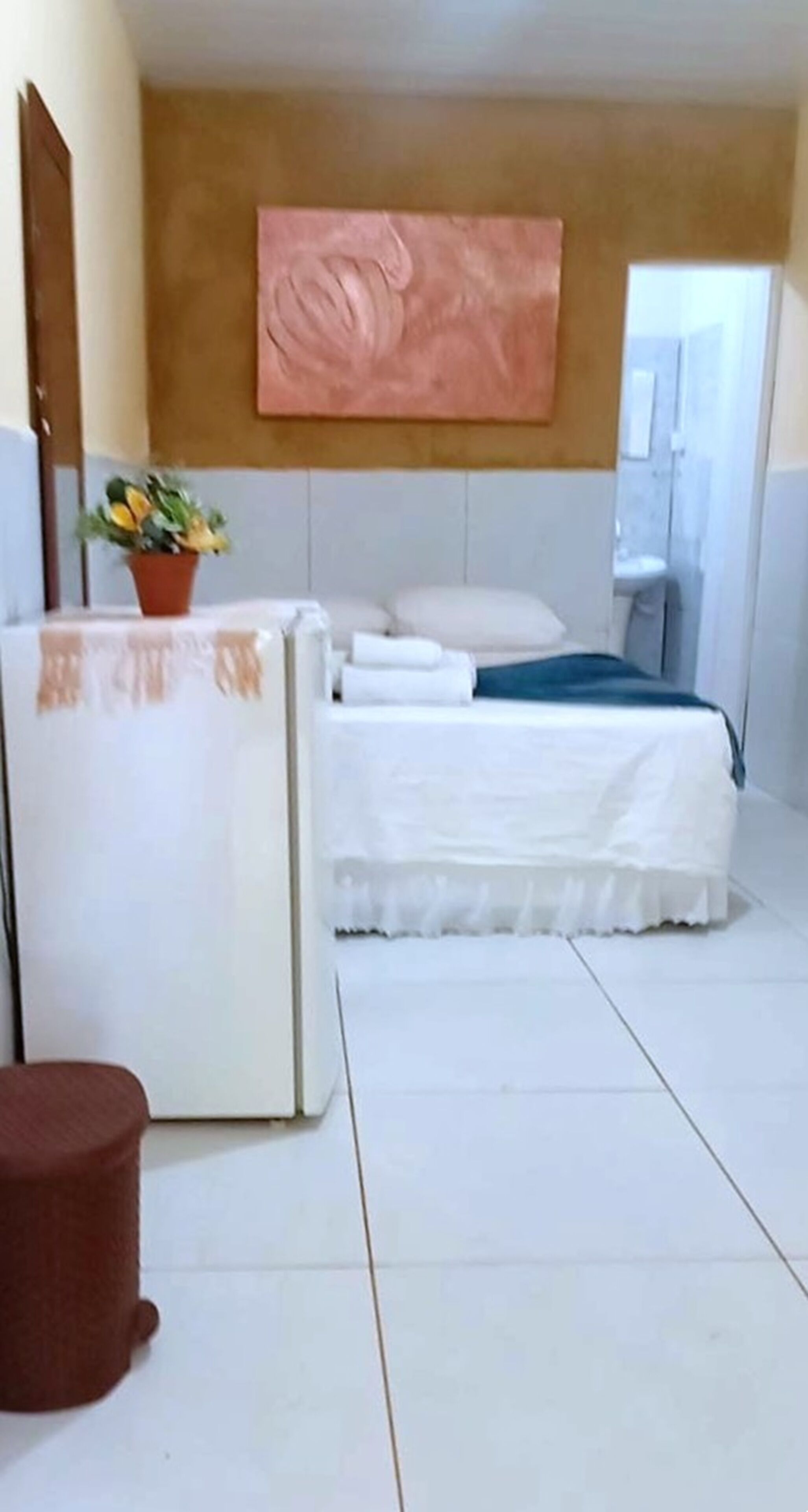 Un dormitorio con una cama, una mesita de noche con una planta en maceta y una obra de arte colgada en la pared.