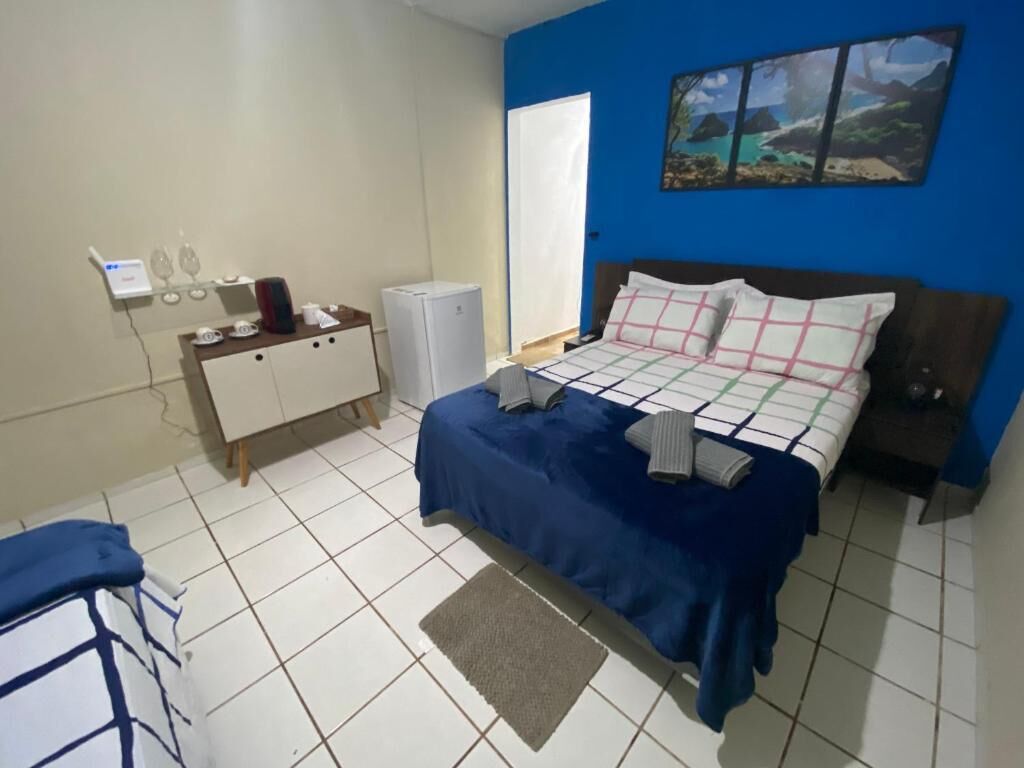 A bedroom with a bed, a desk with a computer, and a refrigerator.