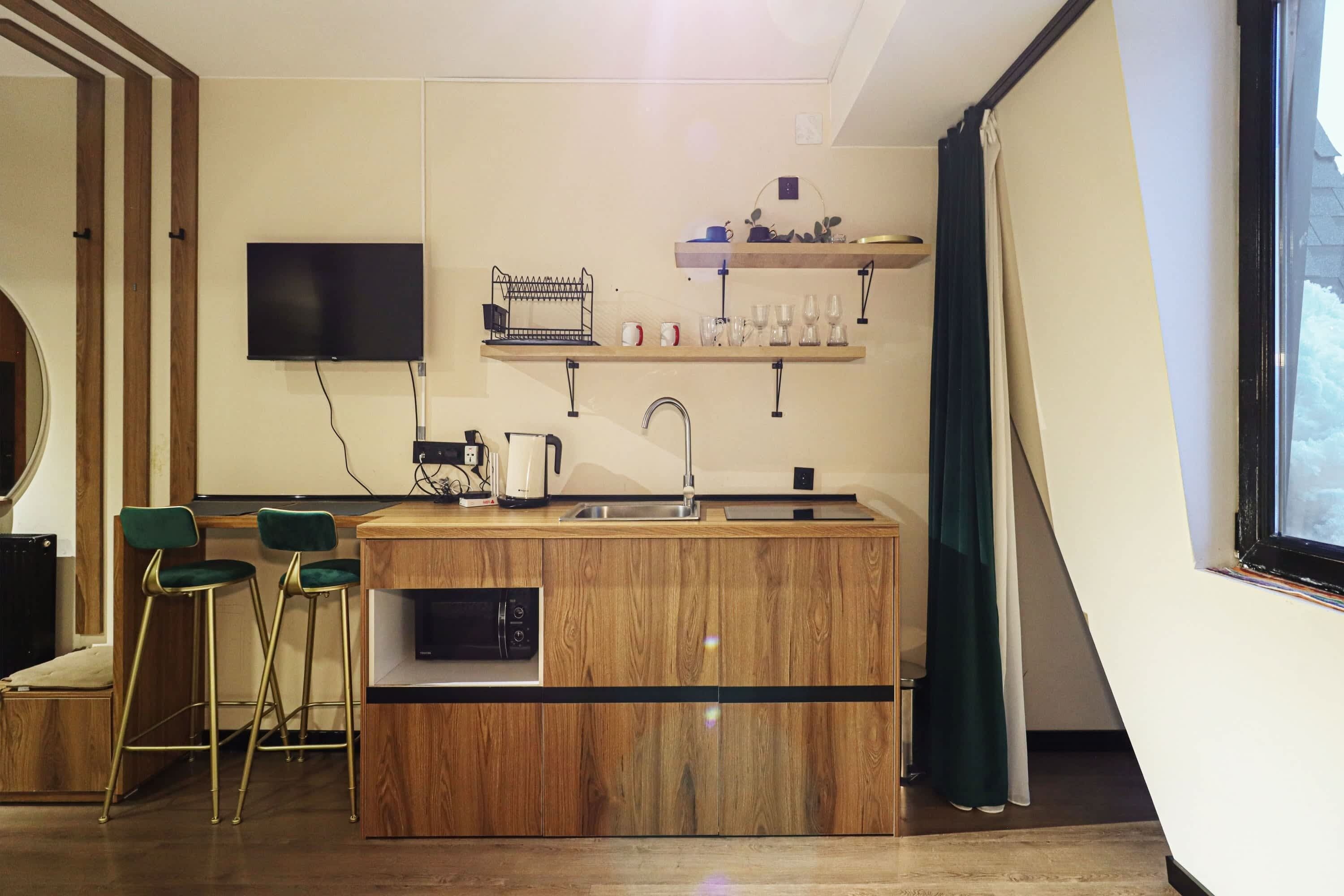 Cuina compacta amb una illa integrada, tamboretes de bar, televisió de pantalla plana i una finestra amb cortines.