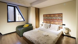 A modern bedroom with a large bed, a green sofa, a window, and a colorful tapestry on the wall. - Charming studio In Marshall Gudauri -By Wehost (Gudauri)
