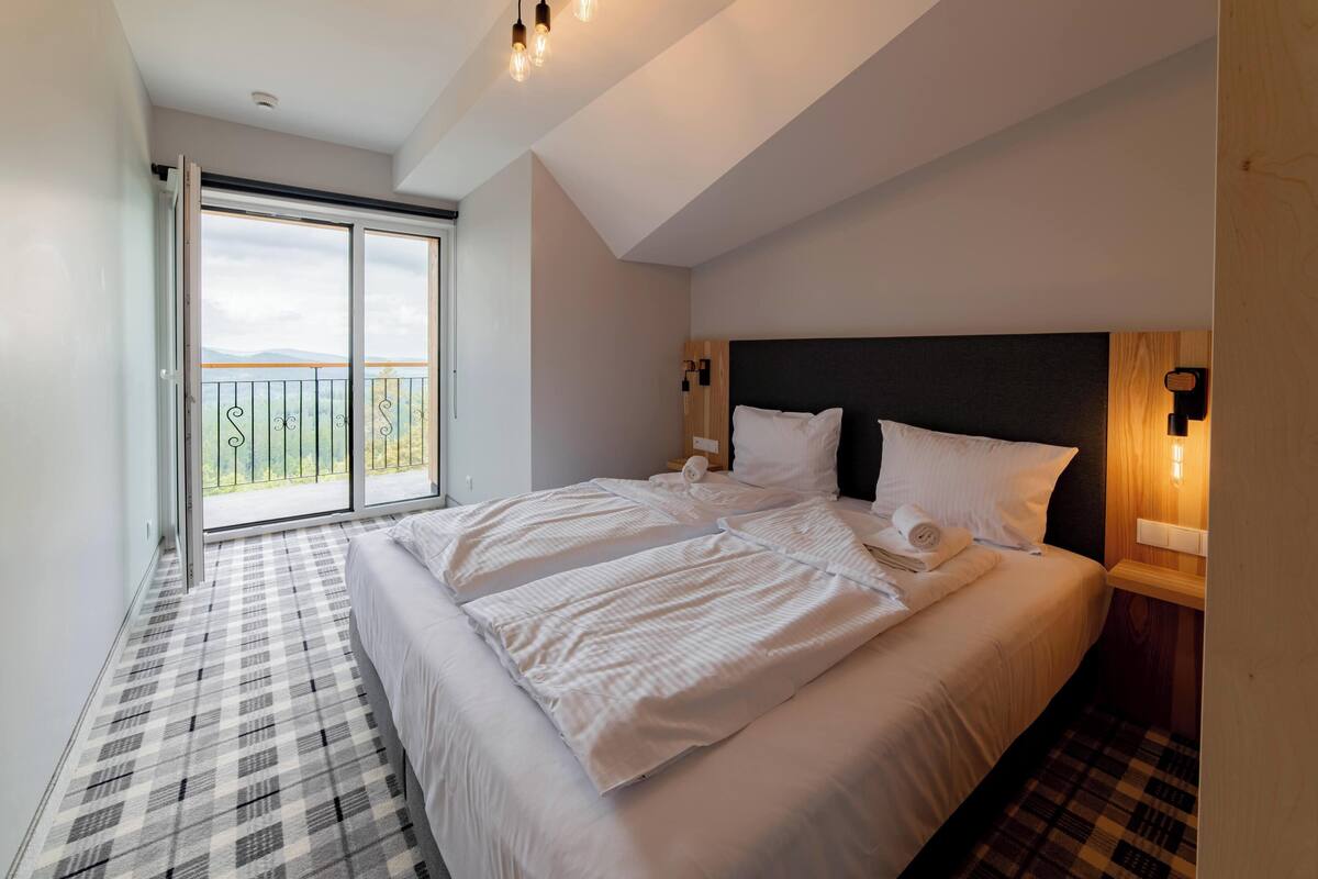 A bedroom with a large bed, a balcony with a view, and a modern design.