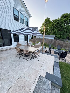 A patio with a table and chairs, a striped umbrella, and a wooden fence. - Modern Farmhouse- Walkable to town: Spacious (Boyne City)