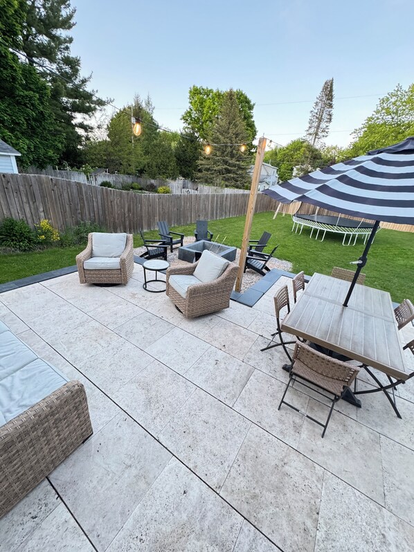 A patio area with wicker furniture, a table, and chairs. There is a wooden fence in the background. - Modern Farmhouse- Walkable to town: Spacious (Boyne City)