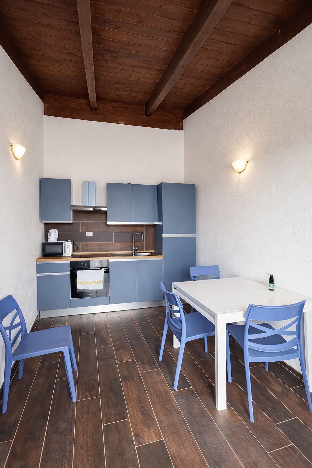 Una cocina compacta con armarios azules, una encimera blanca y un comedor con sillas azules.