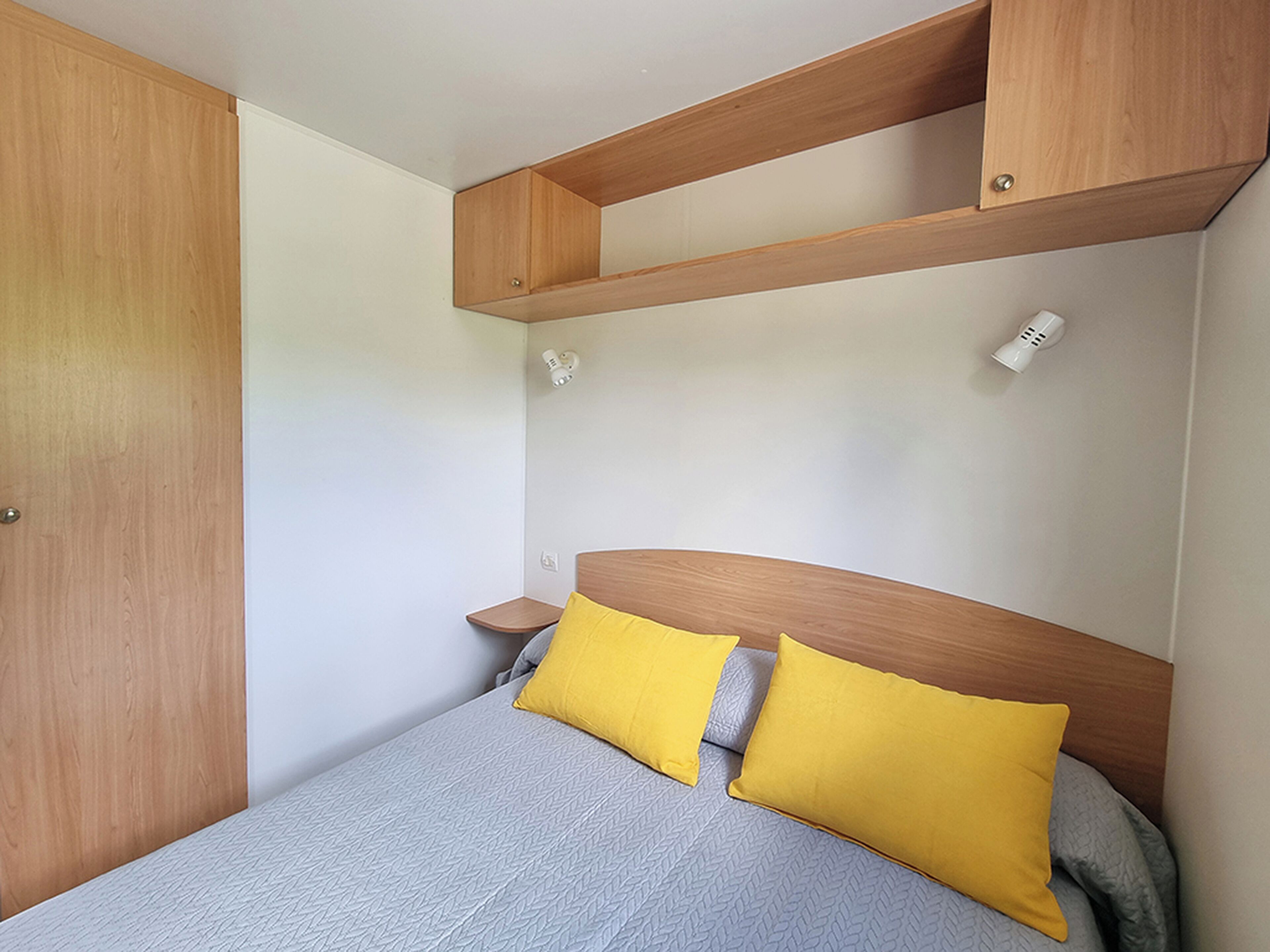 Un dormitorio con cama, cabecero de madera, dos mesitas de noche y un armario.