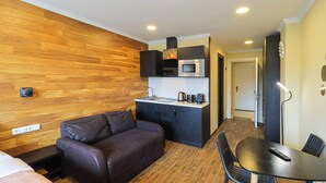 Habitación compacta con pared de madera, un sofá, una pequeña kitchenette y un comedor.