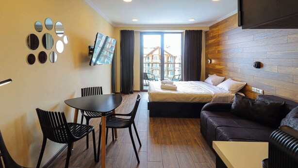 Una habitación de hotel con cama, sofá, mesa de comedor con sillas y televisor fijado a la pared.