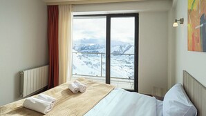 Et hotelværelse med en seng, et vindue der viser udsigt til sneklædte bjerge, en radiator og et billede på væggen.