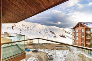 A modern building with a glass balcony overlooking a snowy mountain landscape and a parking area. - Modern 2BR Ski Apt in New Gudauri - by Wehost (Gudauri)
