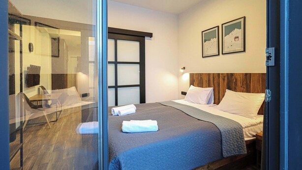 A hotel room with a bed, a desk, and a chair. There are two framed pictures on the wall. - Brand New Ski 1BR Apt In New Gudauri - By Wehost (Gudauri)
