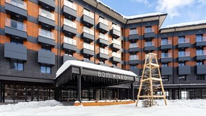 Un hôtel moderne à l’architecture imposante, avec plusieurs étages, une entrée abritée et un terrain enneigé.