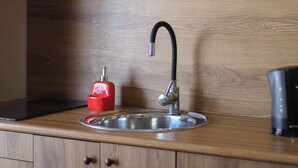 Een keukenkraan met een moderne kraan, een rode zeepdispenser en een waterkoker op het aanrecht.