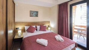 Een hotelkamer met een groot bed, een houten hoofdbord, een nachtkastje met een lamp, een schilderij aan de muur en uitzicht door een glazen deur op een buitenruimte.