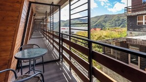 Een balkon met uitzicht op een bergachtig landschap, een tafel en stoelen.