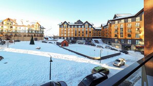 Un estacionamiento cubierto de nieve con varios autos, un pequeño edificio rojo y edificios residenciales de varios pisos al fondo.