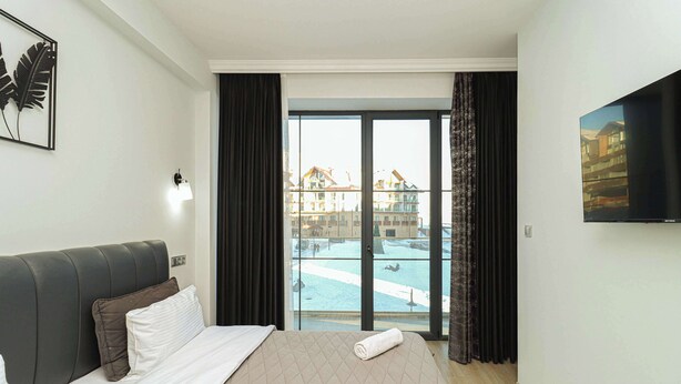 Habitación de hotel con cama, televisión de pantalla plana, ventana con vista a una piscina y edificios.
