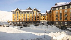Un hotel con varios pisos, balcones y un estacionamiento cubierto de nieve.