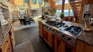 A log cabin kitchen with a central island stove, wooden cabinets, and a dining area with a table and chairs. - Sunrise Ridge – Lake & Mountain View Luxury (Blue Ridge)