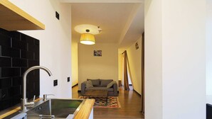 Eine moderne Küche mit Spüle aus Edelstahl und Holz Arbeitsplatte, ein graues Sofa im Wohnbereich und eine hängende Leuchte.
