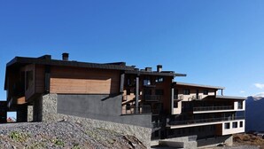 A modern multi-story building with a stone base, wooden upper floors, and balconies. - Modern Mountain Retreat in Gudauri – By Wehost (Gudauri)