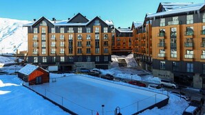 Ett modernt hotell med flera våningar, stora fönster och en snötäckt parkeringsplats.