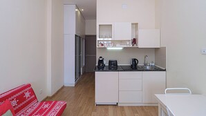 A compact kitchen with white cabinets, a black countertop, and a sink. There is a red patterned sofa in the living area. - Charming New Gudauri Studio - by Wehost (Gudauri)