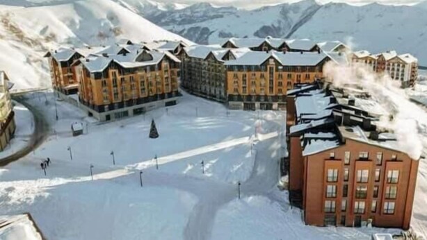 Ein schneebedecktes Resort mit mehreren Gebäuden, einer Skipiste und einem Berg im Hintergrund.