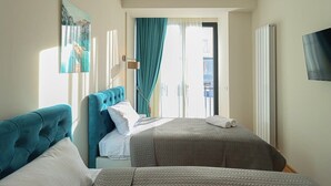 Ein Hotelzimmer mit zwei Betten, einem großen Fenster mit Vorhängen, einem Wand-Fernseher und einer Heizung.
