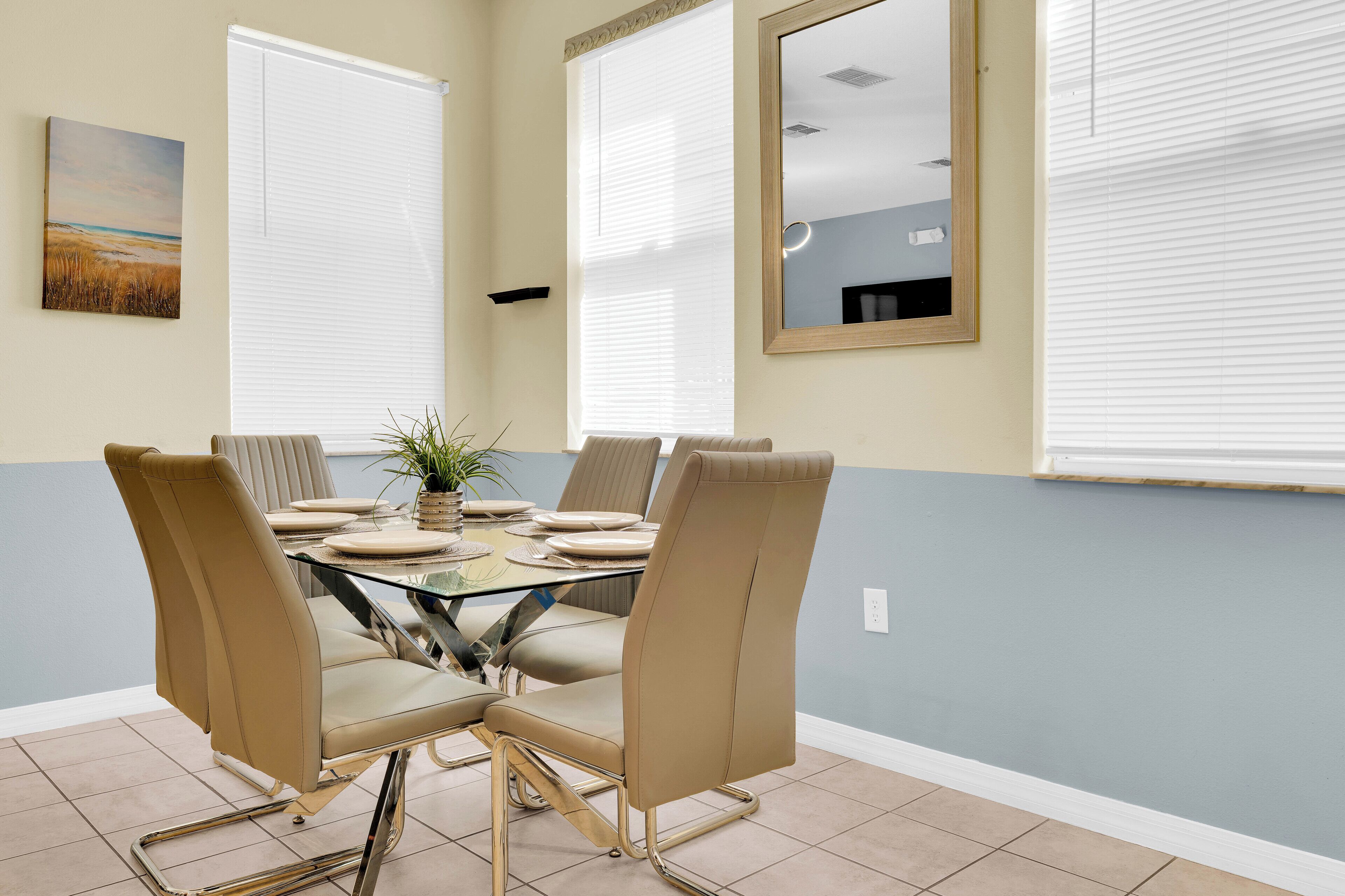 A conference room with a glass table, beige chairs, a potted plant, and a painting on the wall.